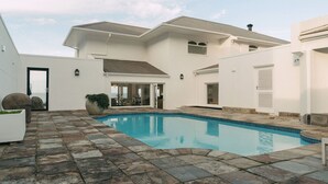 A modern house with a swimming pool, stone patio, and a large window overlooking the pool. - Links Crescent | Contemporary Coastal Sanctuary (Cape Town)