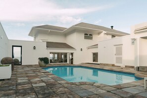 Una casa moderna con piscina, patio de piedra y un amplio ventanal con vistas a la piscina.