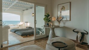 A room with a view of the sea, a bed, a table with a lamp, and a bull skull decoration. - Links Crescent | Contemporary Coastal Sanctuary (Cape Town)
