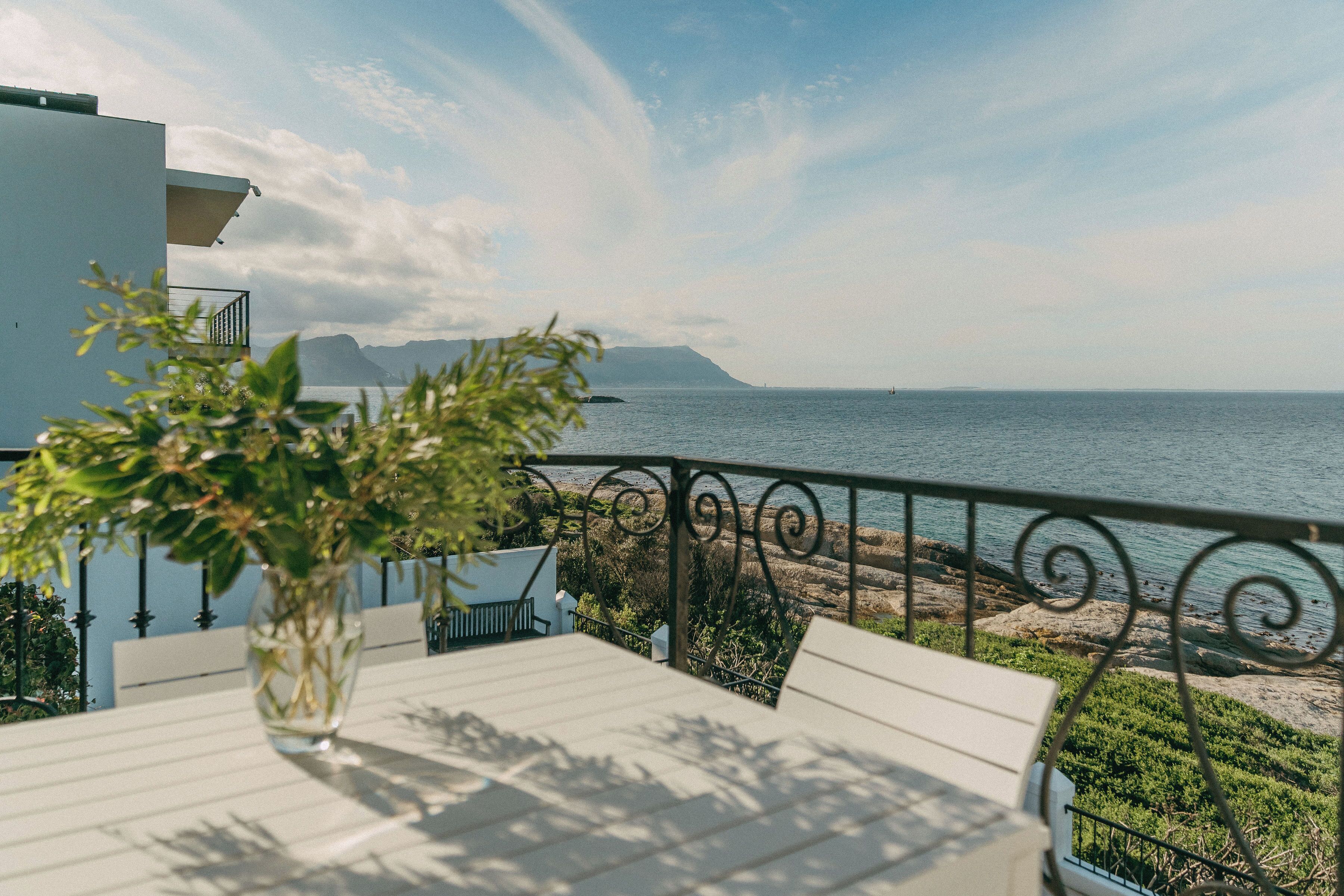 A balcony with a table and chairs, overlooking a beach and the sea.