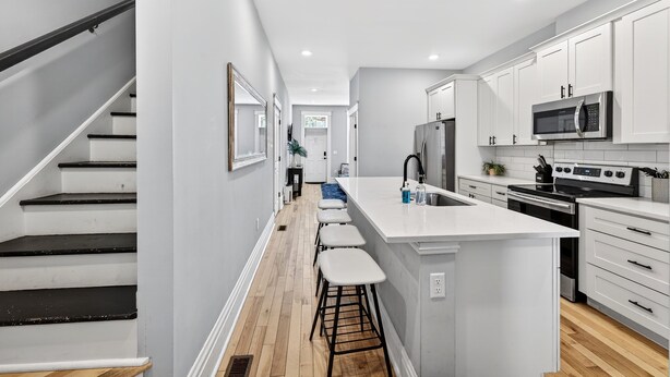 A modern kitchen with white cabinetry, a central island with stools, a microwave, and a stove. - 7Br Group Haven: Yard • Fire Pit • 3 Kitchen (St. Louis)