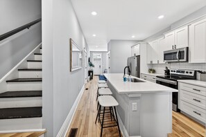 Une cuisine moderne avec des meubles blancs, un îlot central doté de tabourets, un four à micro-ondes et une cuisinière.
