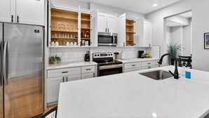 A modern kitchen with white cabinetry, a stainless steel refrigerator, a microwave, an oven, and a sink. - 7Br Group Haven: Yard • Fire Pit • 3 Kitchen (St. Louis)