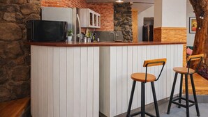 Una cucina con parete in pietra, mobili bianchi e piano di lavoro in legno. Sono presenti due sgabelli da bar e un forno a microonde.