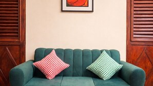 Un divano color petrolio con cuscini a quadretti, un tavolino da caffè nero con ciotole, e un quadro appeso al muro.