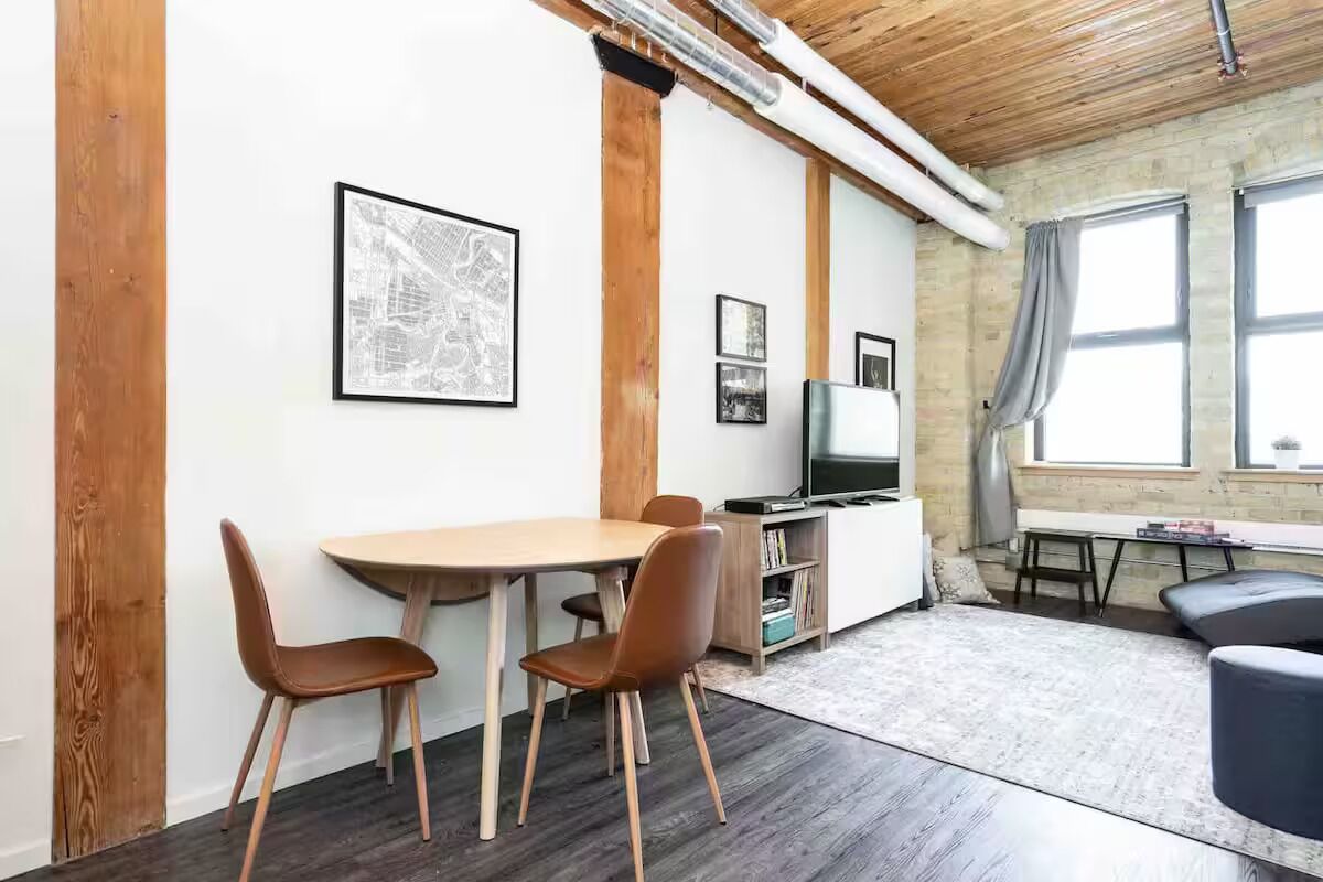 A modern room with a wooden ceiling, a dining table with chairs, a TV, and a large window.