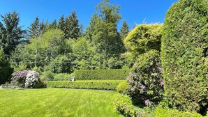 Ein gepflegter Garten mit ordentlich geschnittenen Hecken, verschiedenen Sträuchern und einem strahlend blauen Himmel.