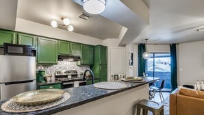 Una cocina moderna con armarios verdes, una isla central y un área de comedor con un sofá marrón.
