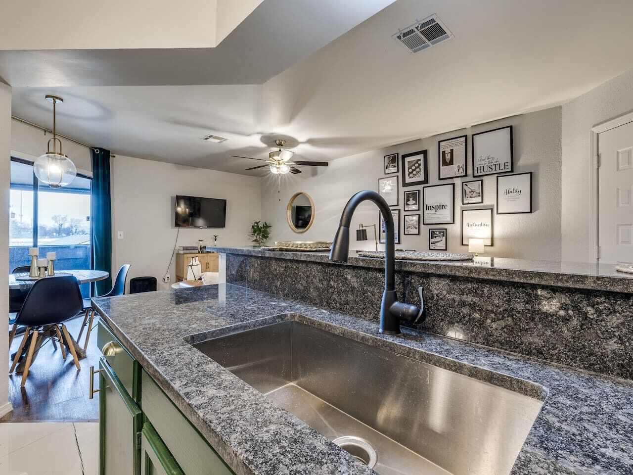 A modern kitchen with a granite countertop, stainless steel sink, and a ceiling fan.