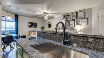 A modern kitchen with a granite countertop, stainless steel sink, and a ceiling fan.
