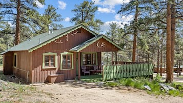 A rustic cabin with a porch, a small deck, and a fenced area.