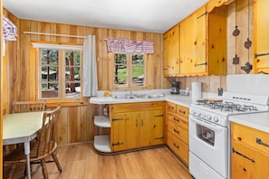 A wooden kitchen with a gas stove, white cabinets, and a window overlooking a garden.