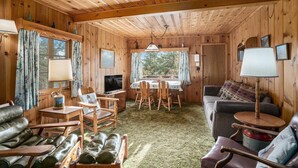 Interior de una cabaña de madera con una mesa de comedor, sillas, un sofá y un televisor.