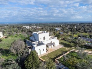 Ein modernes, weißes Haus mit Flachdach, umgeben von Grün und freiem Blick auf das Meer.