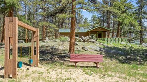 Un tobogan de fusta, una cadira vermella i una cabana amb teulada verda en una zona boscosa.