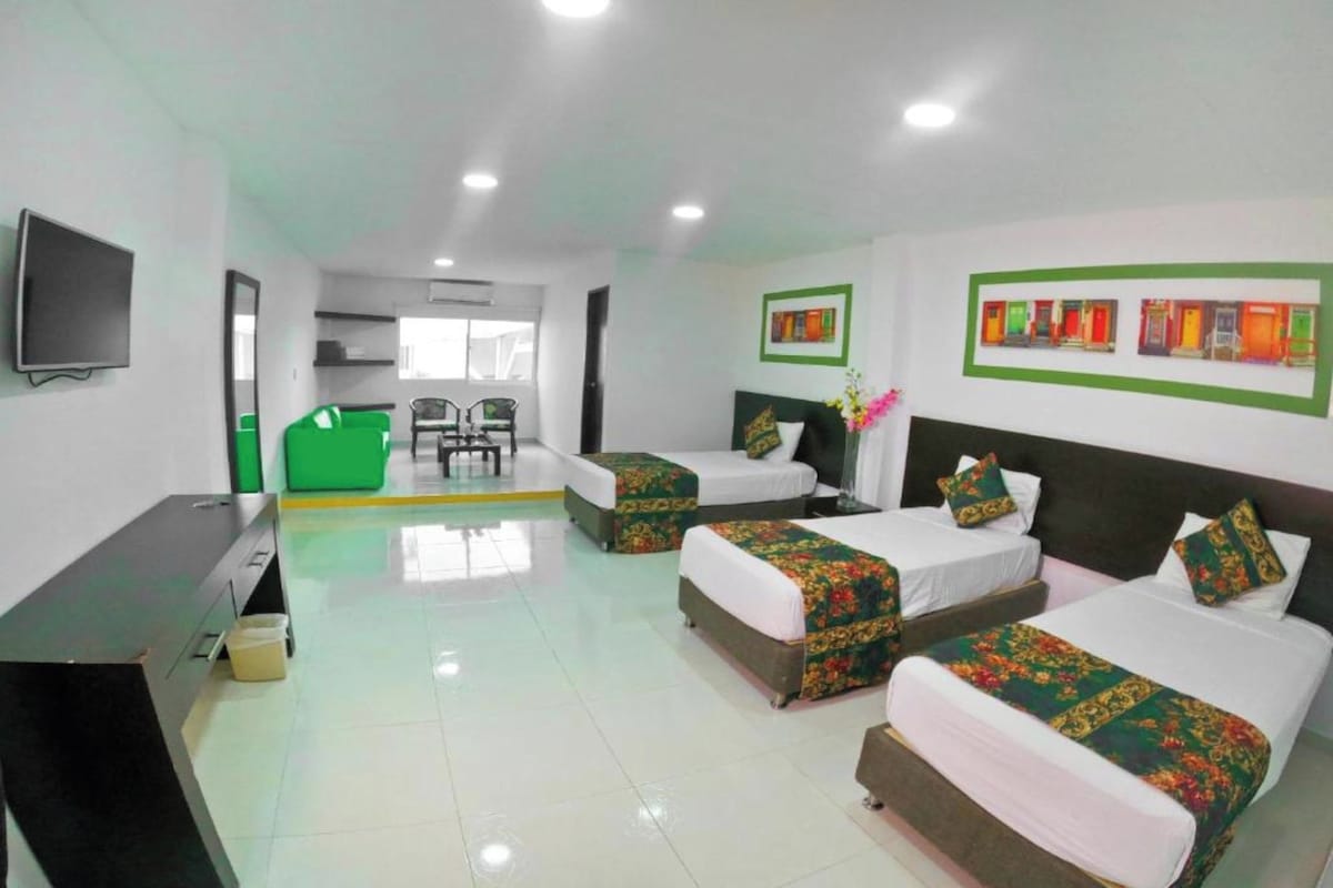 A hotel room with three beds, a desk, a TV, and a green sofa.