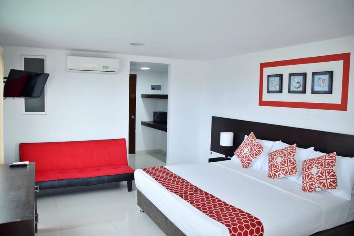Una habitación de hotel con una cama, un sofá rojo, un televisor y cuadros en la pared.