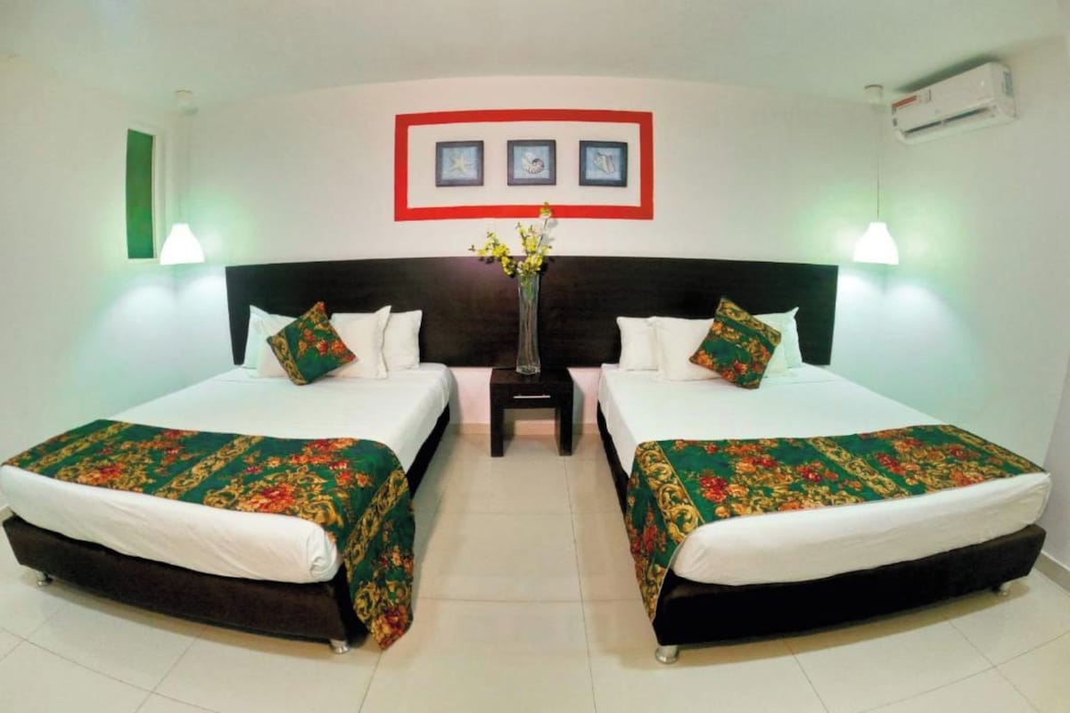 A hotel room with two beds, a nightstand, a vase with flowers, and framed pictures on the wall.