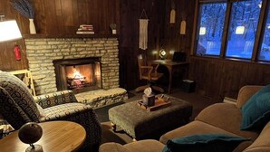 Un salon chaleureux avec une cheminée en pierre, des meubles en bois et une vue sur un paysage enneigé par les fenêtres.