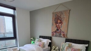 Hotellihuone, jossa on kaksi sänkyä, suuri ikkuna, taulu seinällä ja riippuvalaisin.