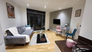 Una sala de estar moderna con un sofá gris, una mesa de centro, una mesa de comedor con sillas y un televisor montado en la pared.