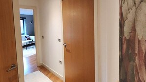 A hallway with wooden flooring, a white door, and a painting on the wall. - Urban Retreat | Leeds City Centre | Sleeps 4 (Leeds)