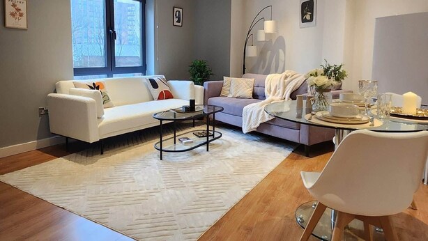 A modern living room with a white sofa, a glass coffee table, and a dining table set for four. - Urban Retreat | Leeds City Centre | Sleeps 4 (Leeds)
