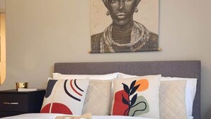 A neatly made bed with white linens and decorative pillows, a bedside table with a book and a candle, and a wall-mounted artwork above the bed. - Urban Retreat | Leeds City Centre | Sleeps 4 (Leeds)