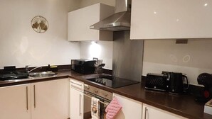 A modern kitchen with white cabinets, a stainless steel range hood, a built-in oven, and a wooden floor. - Urban Retreat | Leeds City Centre | Sleeps 4 (Leeds)