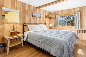 Una habitación con paneles de madera, una cama, lámparas de noche, una mesita y un ventanal con cortinas.