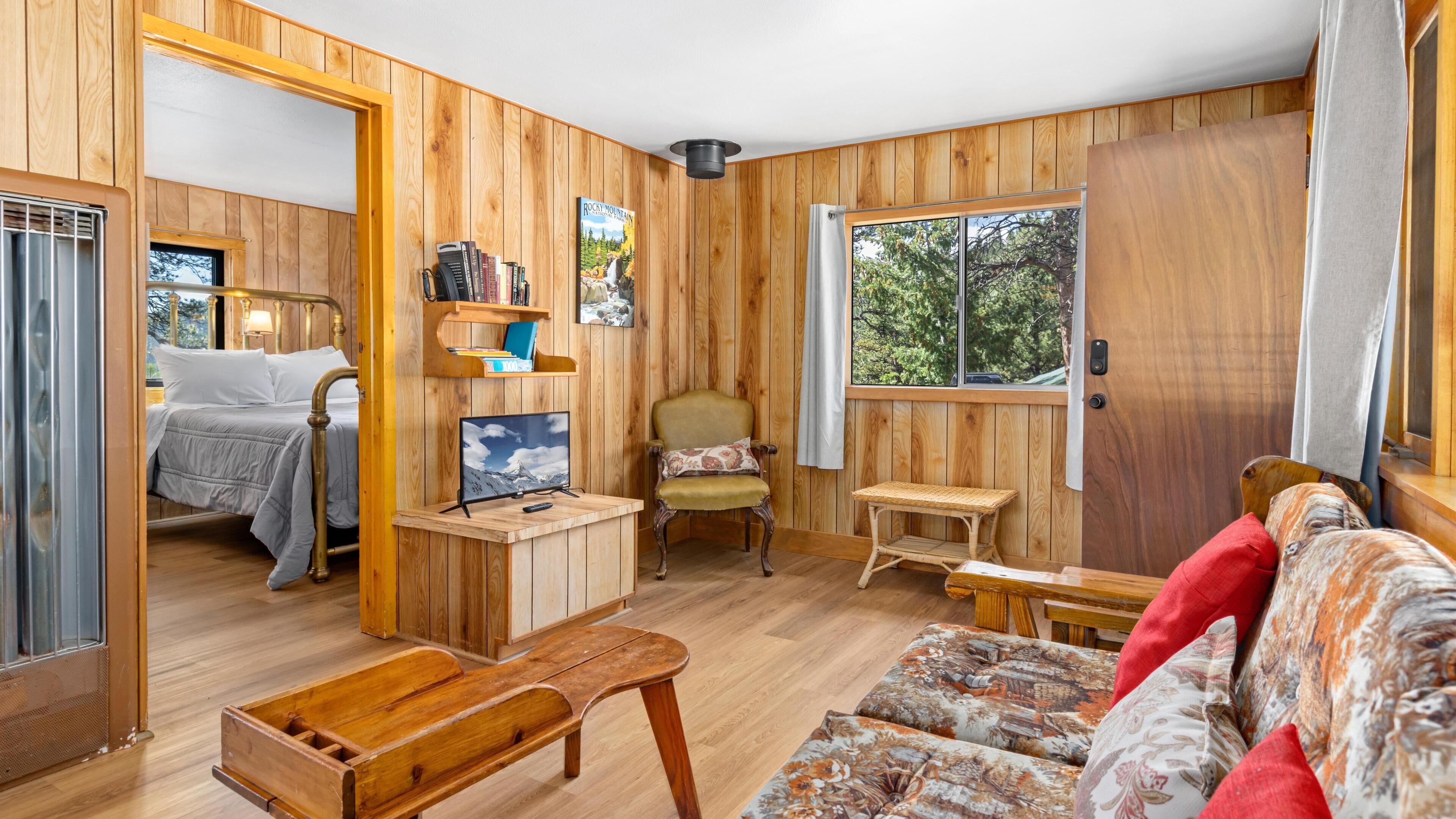 A cozy room with a bed, a wooden chair, a small table, a sofa, and a window with a view of trees.