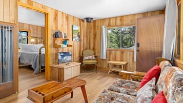 A cozy room with a bed, a wooden chair, a small table, a sofa, and a window with a view of trees.