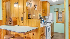 A kitchen with wooden walls, a stove, a sink, and two stools. - Machin's Cottage #7 is calling! Pet Friendly (Estes Park)