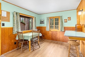 A wooden interior with a dining table, chairs, a bar area, and a window with curtains.