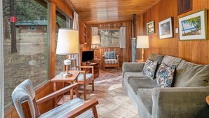Ein gemütliches Blockhaus-Interieur mit Holzwänden, einer Couch, einem Esstisch mit Stühlen und einem Fernseher.