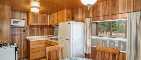 Una cocina compacta con armarios de madera, microondas, refrigerador y una mesa de comedor con mantel a cuadros.