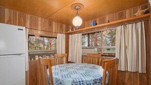 Ein Zimmer mit Holzwänden, einem für vier Personen gedeckten Tisch, einem Kühlschrank und einem Fenster mit Vorhängen.