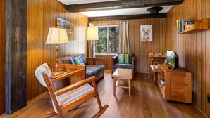 Un intérieur en bois comprenant un canapé, des fauteuils, une table, un téléviseur et une bibliothèque.