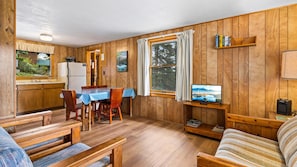 A wooden-paneled room with a dining table, chairs, a television, and a sofa.