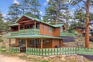 A two-story wooden cabin with a balcony, surrounded by trees.
