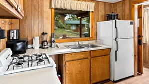 Une cuisine avec des meubles en bois, un réfrigérateur blanc, une cuisinière et une fenêtre donnant sur une maison.