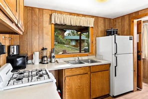 A kitchen with wooden cabinets, a white refrigerator, a stove, and a window with a view of a house.
