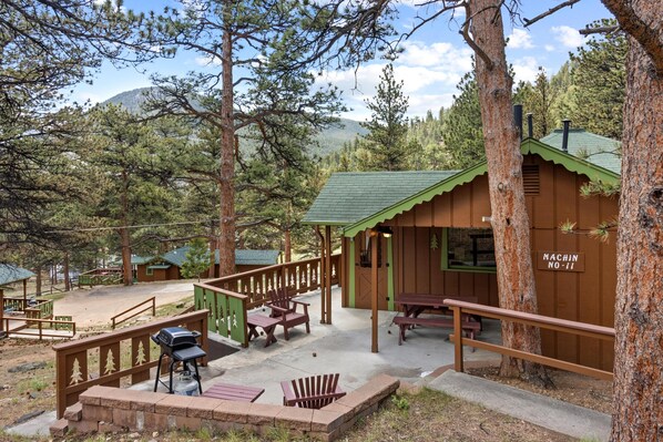 A cabin with a green roof, wooden deck, and picnic tables.