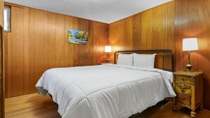 A single bed with a white bedspread in a room with wooden walls and a wooden floor.