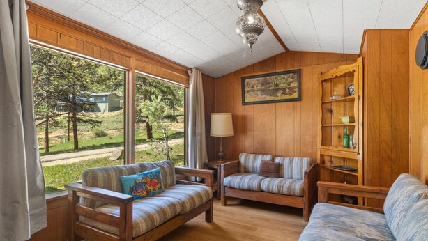 A cozy room with wooden walls, a large window, two sofas, a lamp, and a bookshelf.
