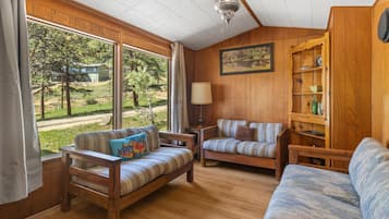 A cozy room with wooden walls, a large window, two sofas, a lamp, and a bookshelf.