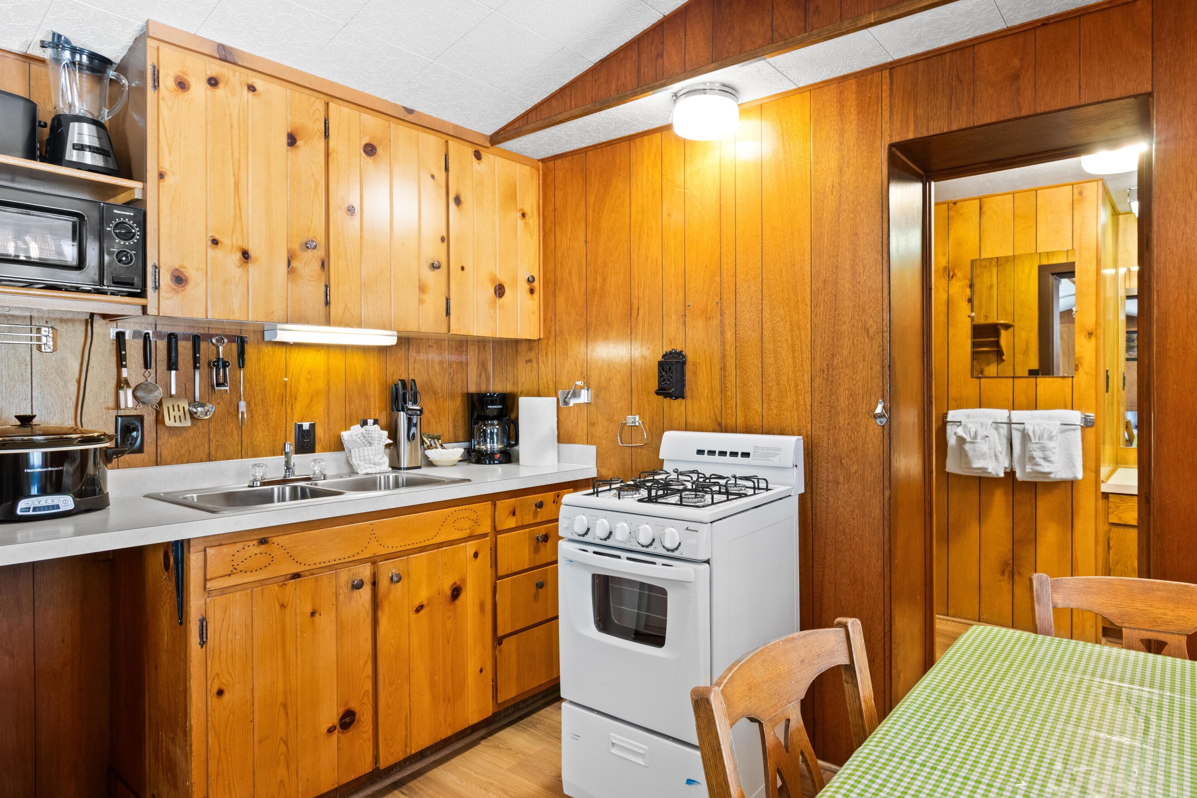 A kitchen with wooden cabinets, a stove, a sink, and a table with a green checkered tablecloth.