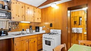 A kitchen with wooden cabinets, a stove, a sink, and a table with a green checkered tablecloth.