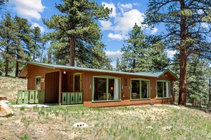 A cabin with a porch, large windows, and a green door, surrounded by trees. - Escape to Machins 14 the heart of nature (Estes Park)