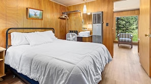 A wooden-paneled room with a bed, a fan, a towel rack, a heater, and a view of the outdoors.